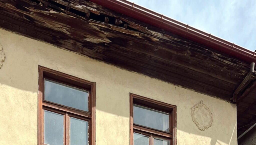 Exterior wall with wood windows and damaged roof trim