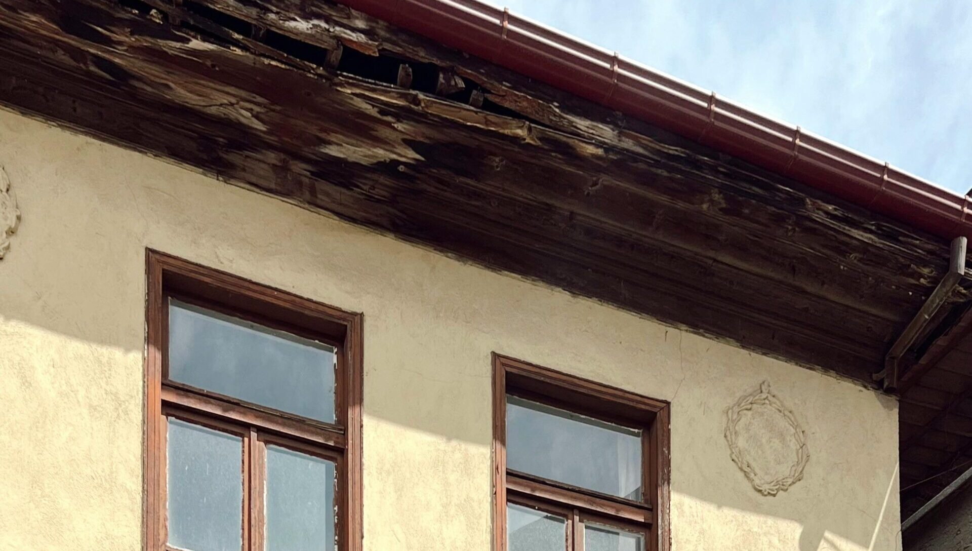 Exterior wall with wood windows and damaged roof trim